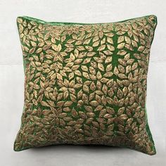 a green and gold decorative pillow on a white wall with an embroidered leaf pattern in the middle