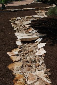 a stone path in the middle of a garden with rocks and mulch on the ground