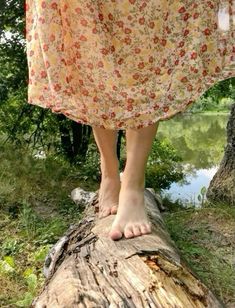 a woman standing on top of a log in front of a tree trunk with her bare feet