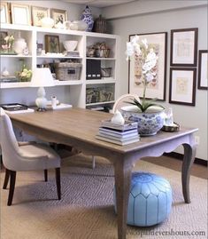 a room with a table, chairs and pictures on the wall above it in front of a bookshelf