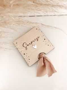 a wooden sign with the word surprise on it and a pink ribbon tied to it