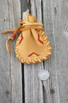 A beaded leather pouch with a drawstring closure is a really sweet gift for all ages. This pouch measures approximately 4 inches tall x 3 inches wide. It is made of soft saddle tan buckskin leather. This leather bag is a great place to keep a special keepsake, your favorite jewelry, medicine stones, or smudge mix. I bead this bag with glass seed beads directly to the leather. The drawstring is decorated with glass crow beads. The props are not included. *Please note leather colors will vary.* Th Native American Clothing, Beadwork Designs, Leather Colors, American Clothing, Sweet Gifts, Bead Leather, Glass Seed Beads