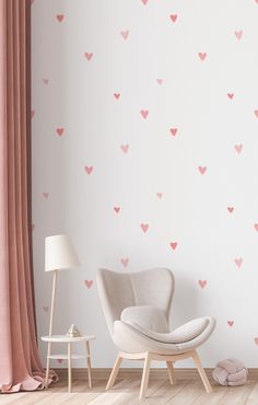 a white chair sitting in front of a wall with pink hearts on it and a lamp