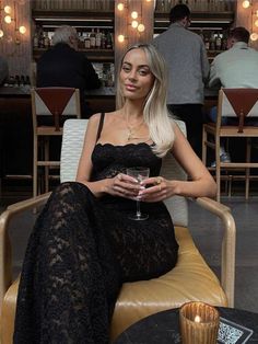 a woman sitting in a chair holding a wine glass and looking at the camera while wearing a black lace dress