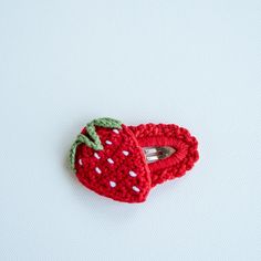 a crocheted strawberry shaped brooch with a green leaf on it's side