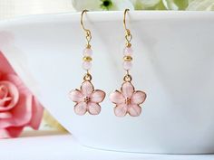 a pair of pink flower earrings sitting on top of a white bowl next to flowers