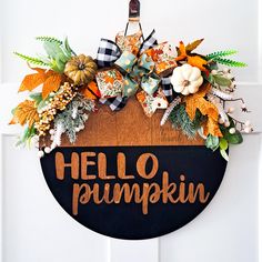 a hello pumpkin sign hanging on the front door with fall leaves and flowers around it