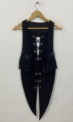 a woman's black vest with white laces hanging on a hanger against a wall