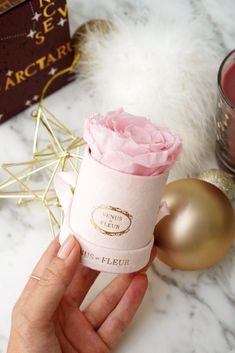 a person holding a pink rose in a gift box next to other christmas ornaments and decorations