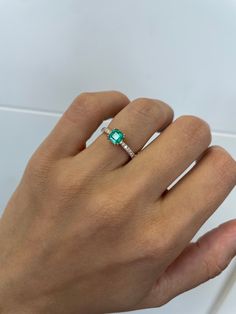 a woman's hand holding an emerald and diamond ring