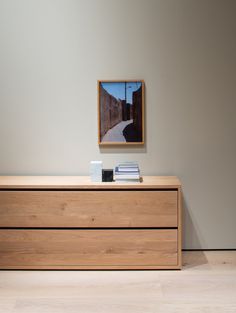 a wooden dresser sitting in front of a wall with a painting hanging on it's side