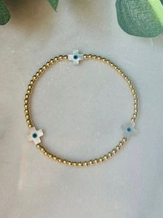 - Cute and dainty evil eye gold beaded bracelet with 18k gold filled beads and white shell cross beads. Excellent stacking addition to other gold beaded bracelets. Coordinating  anklet in shop. Bracelet is beaded on high quality stretch cord. - The evil eye is said to guard against misfortune and believed to protect the person who wears it from any ill-will. **evil eye on cross is very small. A true minimalist look** - 3mm 18k gold filled beads   10x8mm shell cross with evil eye    - Each purchase is sent in a velvet drawstring jewelry bag making the perfect gift for someone special or just for you. - To care for your bracelet, please roll on and off the wrist. Repeated stretching can wear the elastic over time. Avoid excessive contact with water and chemicals. Keep stored in jewelry bag. Adjustable Gold Beaded Cross Bracelets, Gold Spiritual Beaded Cross Bracelets, Gold Beaded Cross Bracelets For Spiritual Style, Gold Cross Beaded Bracelets For Spiritual Style, Spiritual Gold Beaded Cross Bracelets, Gold Cross-shaped Spiritual Beaded Bracelets, Gold Evil Eye Bracelet With Spacer Beads, Gold Evil Eye Bracelet With Round Spacer Beads, Gold Spiritual Evil Eye Bracelet Hand-strung