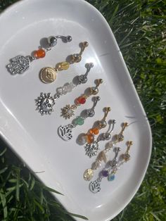 a white tray with many different types of earrings on it in the middle of some grass