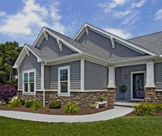 a gray house with white trim on the front door and windows, grass in front