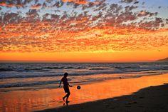 a person running on the beach with a ball in their hand and sunset behind them