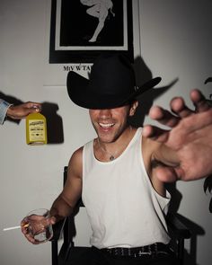 a man wearing a cowboy hat and holding a glass in one hand while another person holds a bottle behind him