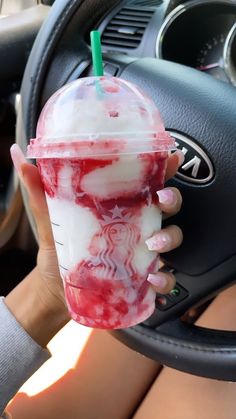 a woman is holding up a drink in her hand while sitting in the driver's seat