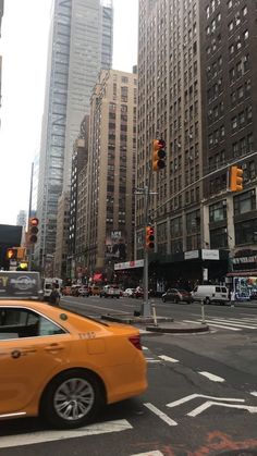 an orange car is driving down the street in front of tall buildings and traffic lights