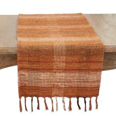 an orange and white table runner on top of a wooden bench with tassels