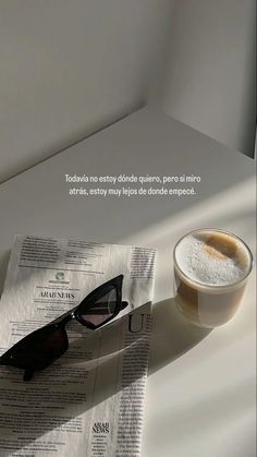 a cup of coffee sitting on top of a newspaper next to a pair of sunglasses