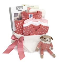 a baby gift basket filled with pink and white clothing, a teddy bear and cardigan