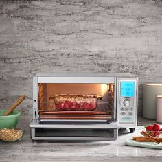 a toaster oven with food cooking in it on a counter next to bowls and utensils