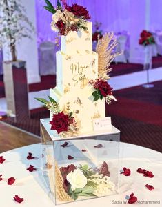 a three tiered wedding cake with red and white flowers on the table at a reception