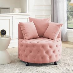 a pink chair sitting in front of a window next to a clock on a table