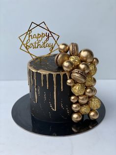 a black and gold birthday cake with icing dripping from it's topper