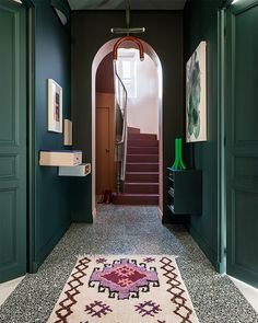 a hallway with green doors and stairs leading to the second floor, along with a rug on the floor