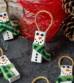 snowmen made out of toilet paper are hanging from twine with pine cones in the background