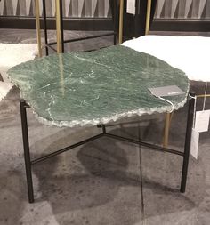 a green marble table sitting on top of a black metal stand in front of other tables