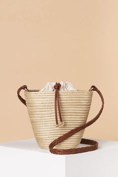 a straw bag sitting on top of a white table next to a brown leather strap