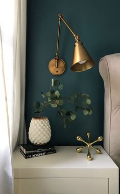 a nightstand with a lamp, potted plant and books on it next to a chair