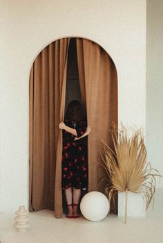 a woman standing in front of a curtain with her hands on the curtains and looking out