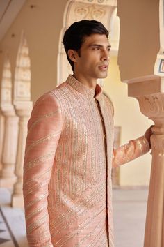 a man standing next to a pillar wearing a pink suit