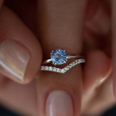 a woman's hand holding a ring with a blue stone in the middle and diamond band around it