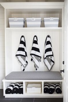 a white bench with black and white towels hanging on it's back wall next to two bins