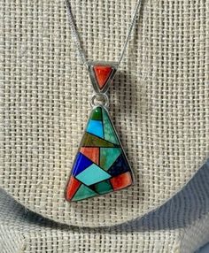 Wow! The colors in this pendant are fabulous and the craftsmanship even better! Hand made and signed by famed Navajo artist, Calvin Begay. So much to love about this pendant. This piece boasts a Modernist style, somewhat askew, triangle shape. The way Calvin has inlaid the different stones in the pendant compliment the shape nicely. Stones include Blue and Green Turquoise, Lapis, Spiny Oyster and Jasper.  The stones sit a bit above the bezel and there is a stone in the bale too! This pendant came to me with this 18" delicate Sterling Silver box chain marked AGI 925. The bale on this piece is large enough to accommodate many thicker styles of chains. The pendant measures 1 1/4" tall x 3/4" wide. The entire necklace weighs .3 oz. Some tarnish and wear on the back of the pendant commensurate Multicolor Southwestern Style Teardrop Jewelry, Multicolor Southwestern Teardrop Jewelry, Southwestern Style Multicolor Teardrop Jewelry, Multicolor Inlay Southwestern Necklace, Collectible Bohemian Multicolor Necklace, Bohemian Multicolor Collectible Necklaces, Multicolor Bohemian Collectible Necklace, Bohemian Multicolor Collectible Necklace, Southwestern Multi-stone Multicolor Jewelry