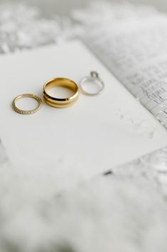 two gold wedding rings sitting on top of an open book next to a pair of diamond earrings