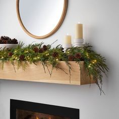 a mantel with candles, pine cones and greenery