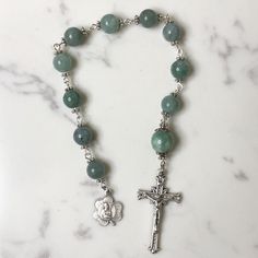 Handmade traditional Catholic single decade tenner rosary using green dyed jade smooth stone round beads. Antique silver daisy bead caps on every bead with additional leaf bead caps on Our Father bead. Antique silver shamrock shaped St. Patrick Pendant with Crosshatch Pattern Crucifix. Hail Mary beads are 8mm with the Our Father bead being 10mm. Designed to be used and/or displayed. Measures about 9.5" long. This rosary would make a beautiful gift for a baby shower, Baptism, First Communion, Confirmation, or any other special event or occasion. Comes in a beautiful black velvet pouch. I ship same or next business day. All of my rosaries are one of a kind and are my own personal creation. Photos are a part of the description-you will receive the exact rosary pictured. Please don't hesitate Adjustable Green Spiritual Rosary, Adjustable Green Rosary With Round Beads, Spiritual Rosary Bracelet With Polished Beads, Green Beaded Spiritual Rosary Bracelet, Spiritual Rosary With Spacer Beads, Green Spiritual Rosary Bracelet With Round Beads, Spiritual Green Rosary Bracelet With Round Beads, Handmade Green Spiritual Rosary Bracelet, Green Beaded Spiritual Rosary