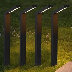 four lights are placed in the grass next to each other on top of some poles