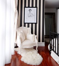 a white chair sitting on top of a hard wood floor next to a black and white striped wall