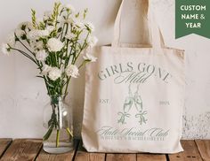 a tote bag sitting next to a vase with flowers in it on a wooden table