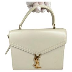 Cream ‘Cassandra’ shoulder bag from Saint Laurent. Made of calf leather. Fastened with a decorative closure featuring a logo in antiqued gold-tone. Half-round handle. Adjustable shoulder strap. Maroon lining. Two compartments and a slip pocket inside. Color: Cream/off white Material: leather Model No.: 578000 Measures: H 7.5” x L 9.5” x D 4” Drop: 3” Comes with: Dust bag and shoulder strap Condition: Goof/fair. Scratches and discoloration throughout. Please ask for more pictures if you’re intere Round Handle, Color Crema, Saint Laurent Bag, White Material, A Logo, Fashion Handbags, Antique Gold, Inside Pocket, Leather Shoulder Bag