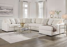 a living room filled with white furniture and large window covered in curtains on the windowsill