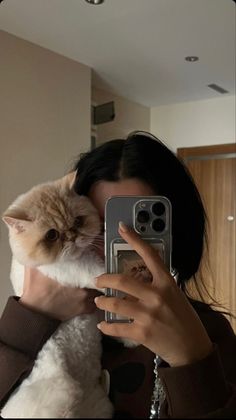 a woman is taking a selfie with her phone while holding a cat in her arms