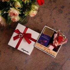 two gift boxes with flowers in them on a table next to a bouquet of roses