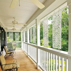 a porch with chairs and ceiling fans on the side of it in front of trees